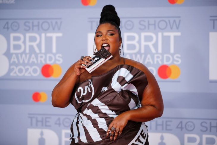 Lizzo usando un vestido con estampado de chocolate y simulando comer su bolso de barra de chocolate 