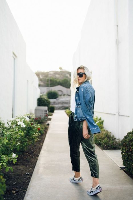 Chica rubia tomada de espaldas con blusa blanca, chamarra de mezclilla y pantalón verde de terciopelo