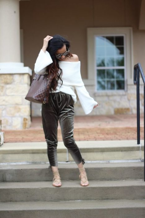 Mujer morena de cabello largo con blusa sin hombros en blanco con pantalón gris de terciopelo