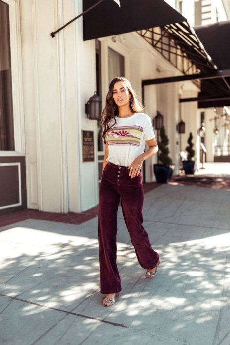 Chica delgada de cabello largo con blusa blanca y pantalón guinda de terciopelo