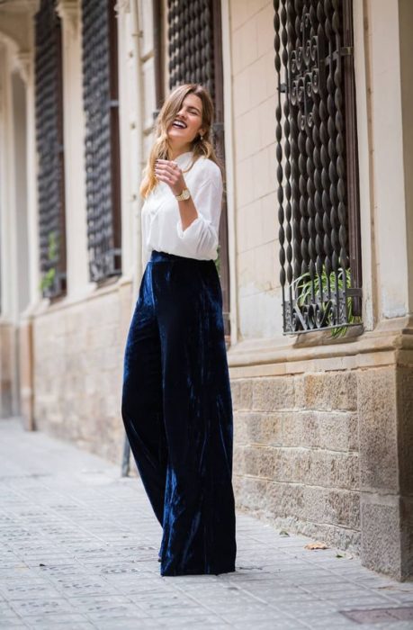 Chica rubia de cabello largo con camisa blanca y pantalón de terciopelo azul