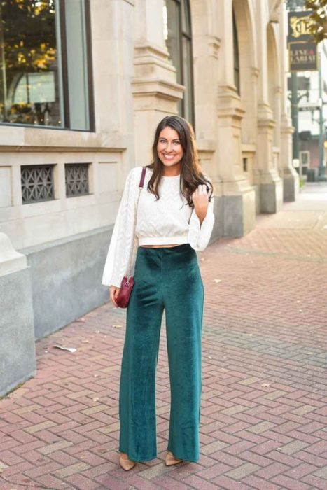 Mujer de cabello oscuro suelto con blusa blanca y pantalón verde esmeralda