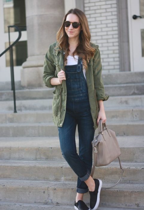 Chica de cabello largo castaño con blusa blanca, overol y chamarra larga verde limitar