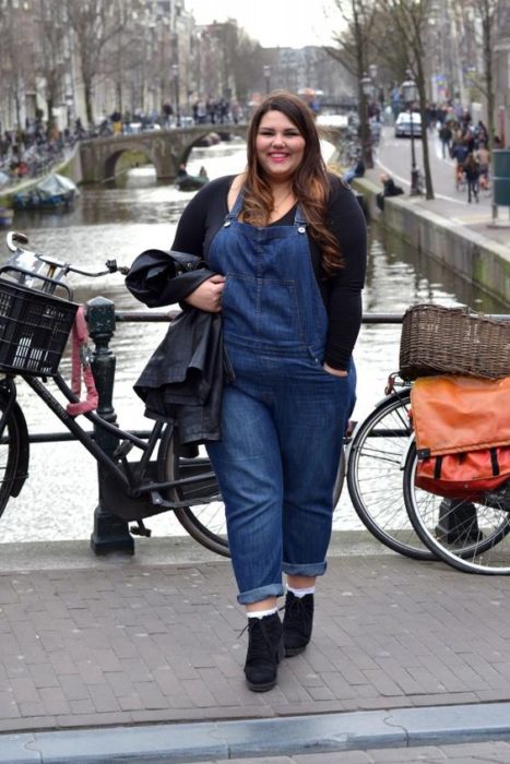 Chica plus size con blusa negra y overol de mezclilla