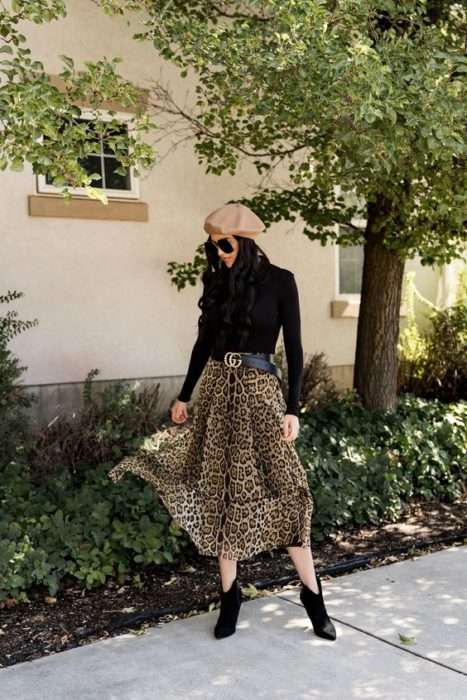 Chica posando con blusa de manga larga negra, gorro beige y maxi falda con estampado de leopardo