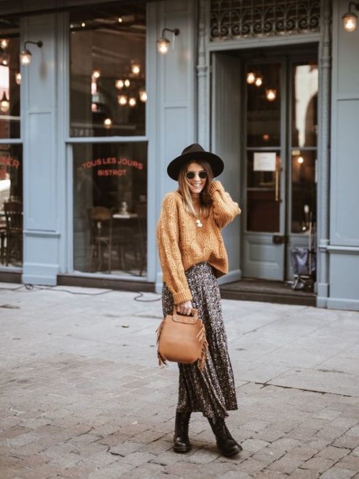 Chica de cabello castaño con sombrero negro, suéter largo color amarillo y maxi falda de animal print