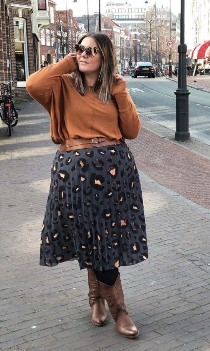 Chica plus size con suéter naranja, maxi falda gris con mancha de leopardo y botas