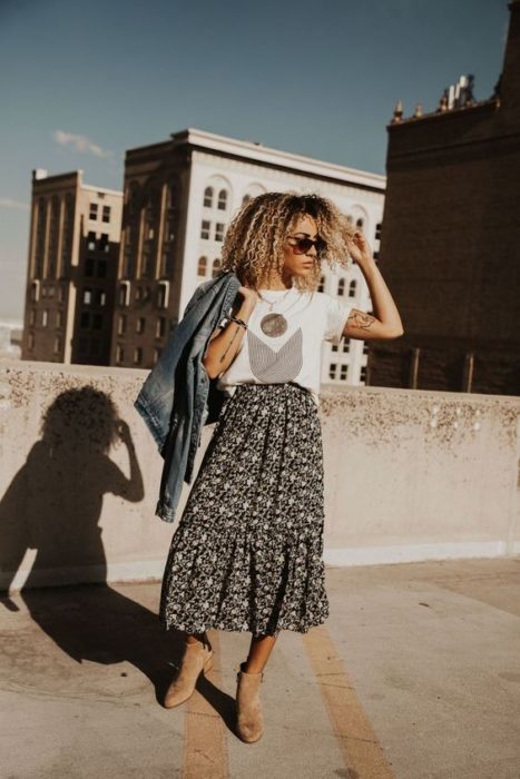 Chica de cabello rizado rubio con blusa blanca y maxi falda de flores con fondo negro