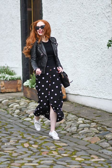 Chica pelirroja con blusa, chamarra y falda negras con tenia blancos