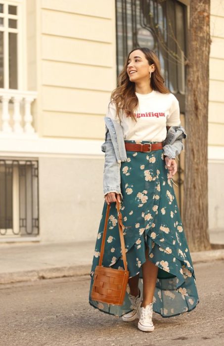 Chica de cabello largo castaño con blusa blanca, suéter gris y falda verde con flores