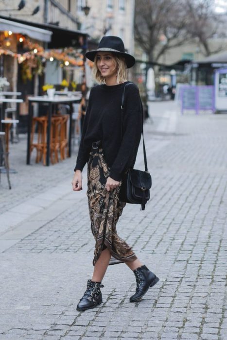 Chica rubia caminando en la calle con sombrero negro, suéter negros, botines negros y maxi falda de leopard print