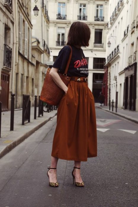 Chica posando en la calle con blusa negra y falda larga color naranja y tacones cafés