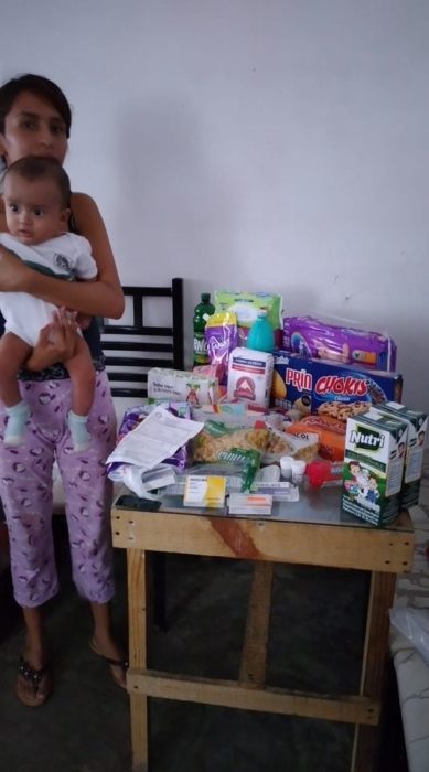 Chica sosteniendo a su bebé y agradeciendo por la despensa que le regalaron