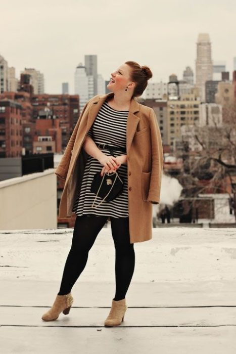 Chica curvy usando botines y sacos camel, con medias y bolsa negro y vestido a rayas negro con blanco