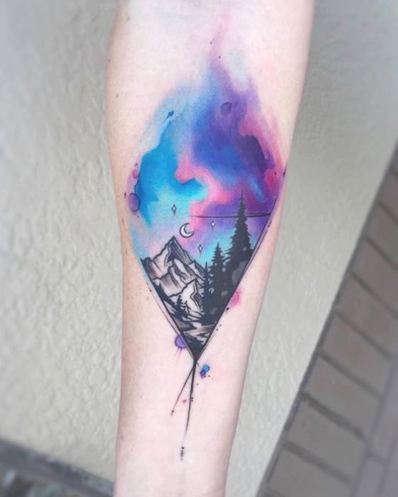 Tatuaje en rombo, de una montaña y árboles con colores de una aurora boreal