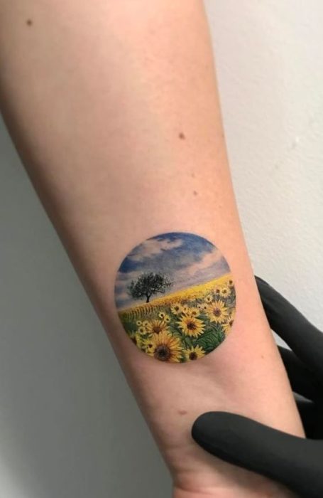 Tatuaje sobre la muñeca de un círculo donde aparece un campo de girasoles