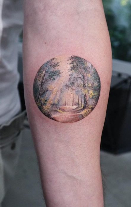 Tatuaje en la parte interna del antebrazo de un camino en el bosque en colores tenues