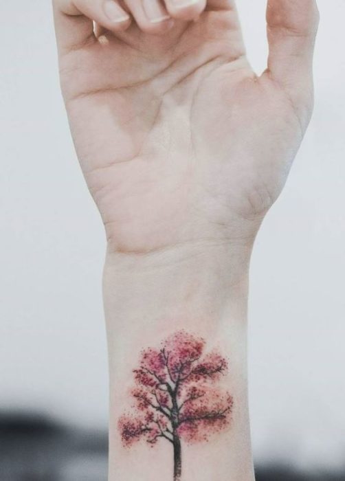 Tatuaje sobre la muñeca de un árbol en tonos otoñales