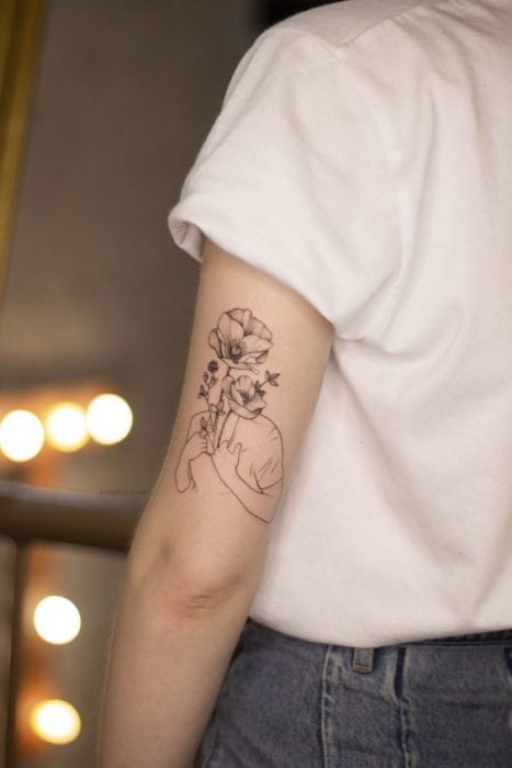 Tatuaje detrás del brazo de la silueta de una mujer con flores en lugar de un rostro