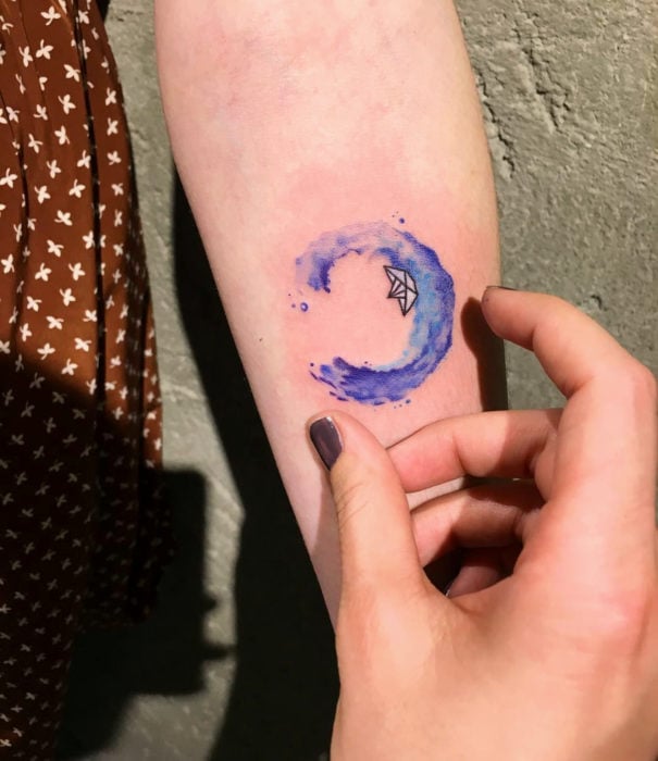 Diseños bonitos de tatuajes de acuarelas; tatuaje de ola con barco de papel en el brazo