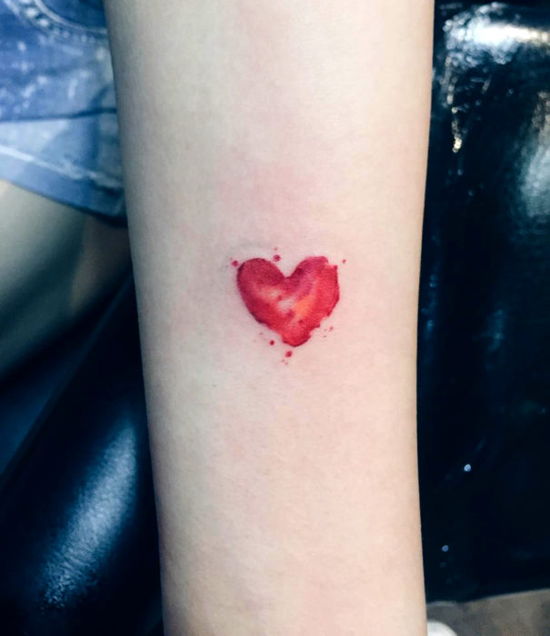 Diseños bonitos de tatuajes de acuarelas; tatuaje de corazón rojo pequeño en el brazo