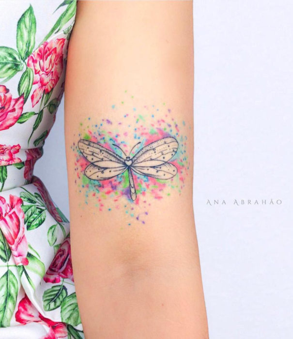 Diseños bonitos de tatuajes de acuarelas; tatuaje de libélula en colores pastel en el brazo