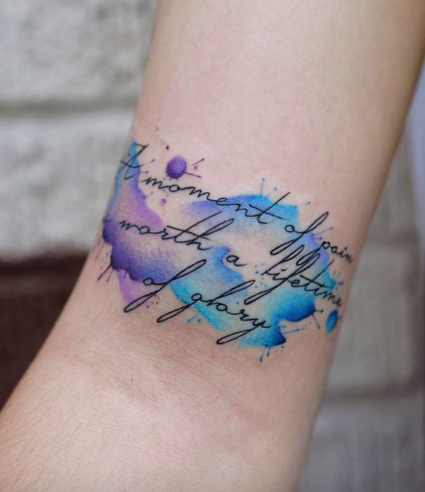 Diseños bonitos de tatuajes de acuarelas; tatuaje de manchas de pintura acuarela con frase en la muñeca