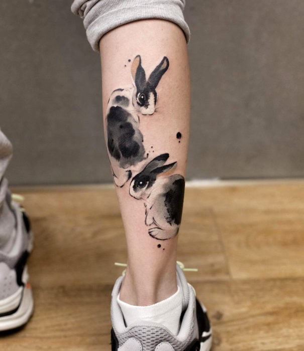 Diseños bonitos de tatuajes de acuarelas; tatuaje de conejos negros en la pierna