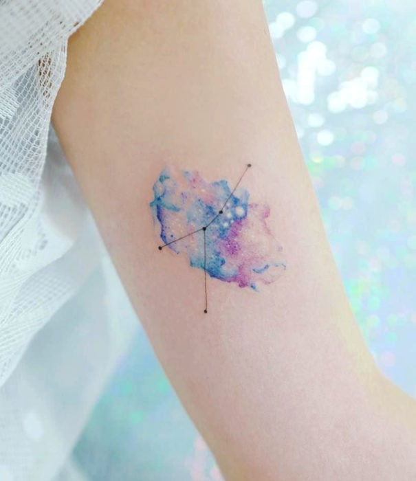 Diseños bonitos de tatuajes de acuarelas; tatuaje de universo y constelaciones en colores pastel en el brazo