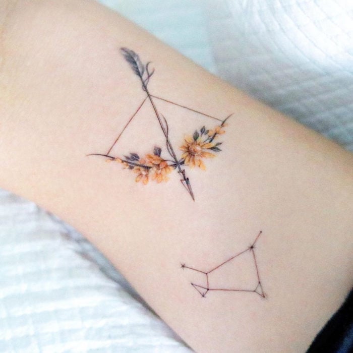 Tatuaje mini, pequeño de flores femeninas amarillas en un arco y flecha en el brazo