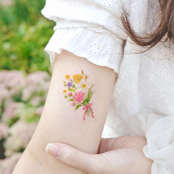 Tatuaje mini, pequeño de flores femeninas amarillas, blancas, rosas y moradas en el brazo