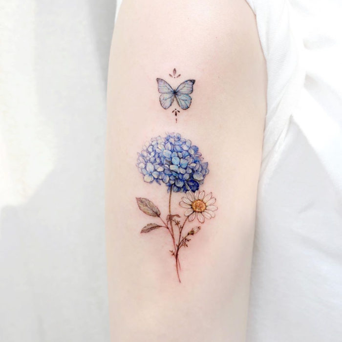 Tatuaje mini, pequeño de flores femeninas hortensias azules y margarita blanca con mariposa en el brazo