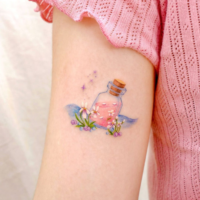 Tatuaje mini, pequeño de flores femeninas blancas con botella con poción, en el brazo