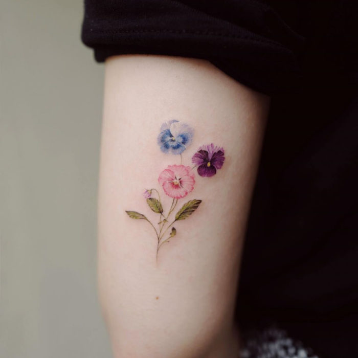 Tatuaje mini, pequeño de flores femeninas pensamientos azules, rosas y morados en el brazo, tríceps