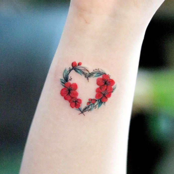 Tatuaje mini, pequeño de flores femeninas rojas formando un corazón en la muñeca