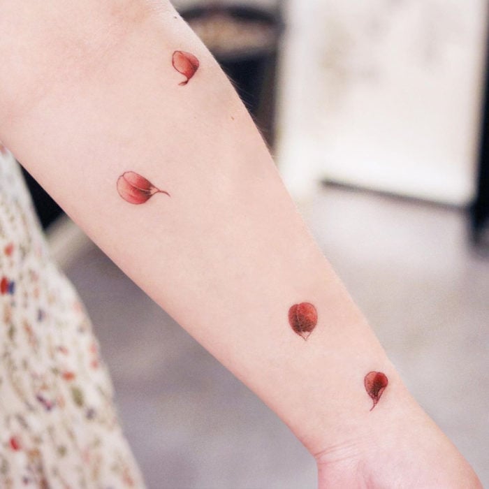 Tatuaje mini, pequeño de flores femeninas rojas, pétalos cayendo en el brazo