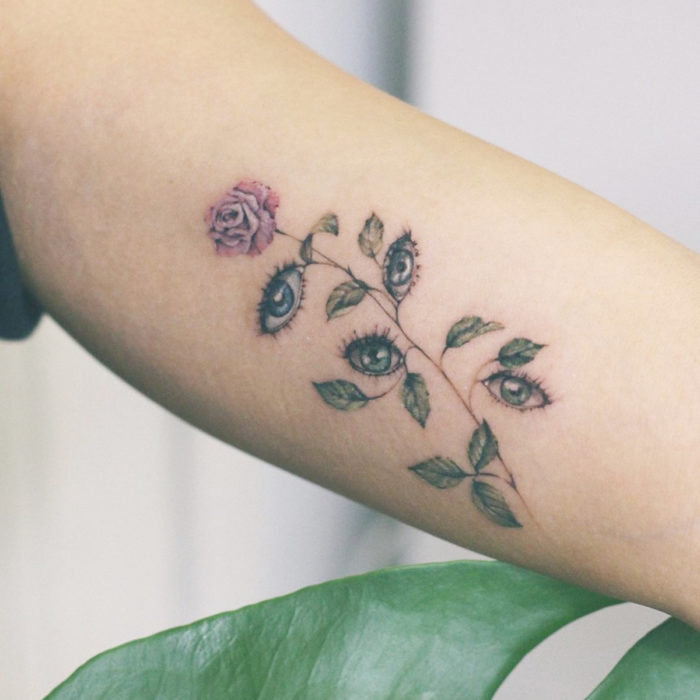 Tatuaje mini, pequeño de flores femeninas rosa con ojos en vez de hojas, en el brazo