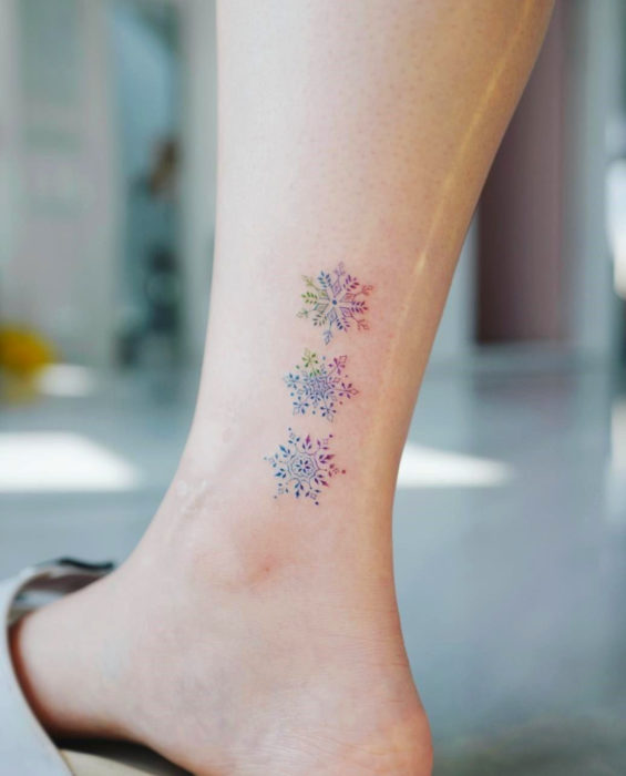 Tatuaje de copos de nieve en colores pastel en el tobillo