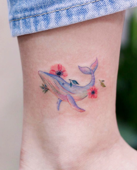 Tatuaje de ballena y flores de cerezo en colores pastel en el tobillo