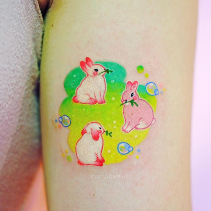 Tatuadora hace tatuajes bonitos, delicados y femeninos que brillan; tatuaje de conejos tiernos color rosa y blanco en el brazo