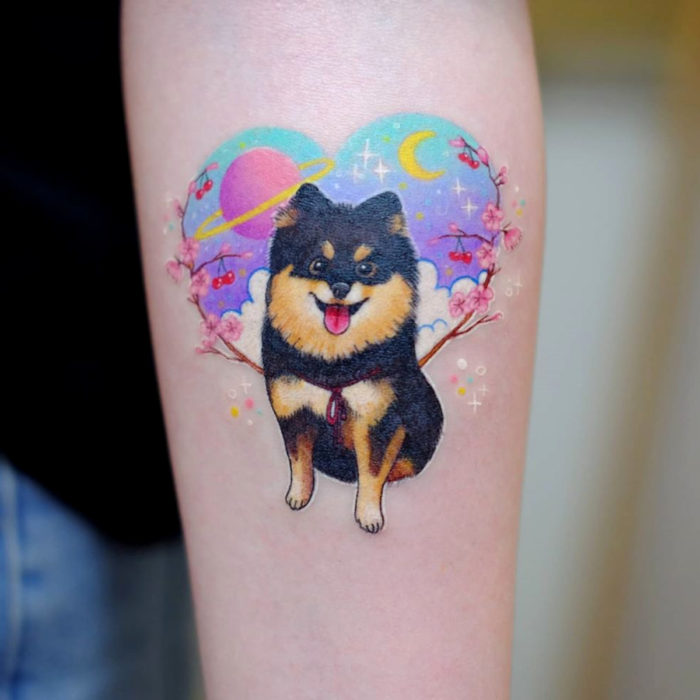 Tatuadora hace tatuajes bonitos, delicados y femeninos que brillan; tatuaje de perro con flores de cerezo, corazón con planetas y Luna en el brazo