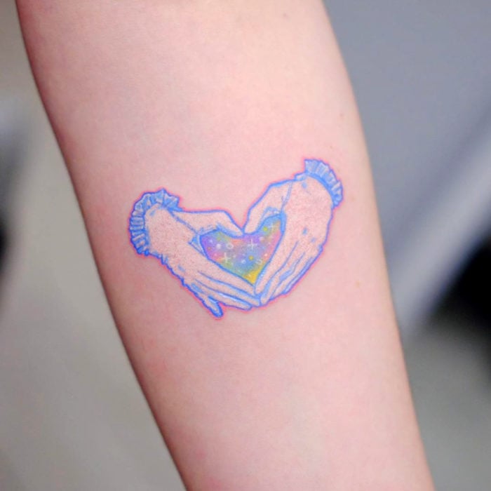 Tatuadora hace tatuajes bonitos, delicados y femeninos que brillan; tatuajes de manos formando un corazón con galaxia de colores pastel en el brazo