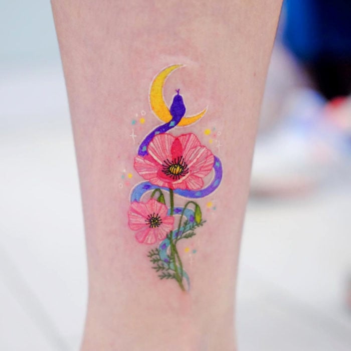 Tatuadora hace tatuajes bonitos, delicados y femeninos que brillan; tatuaje de flores rosas con serpiente morada y Luna amarilla en el brazo