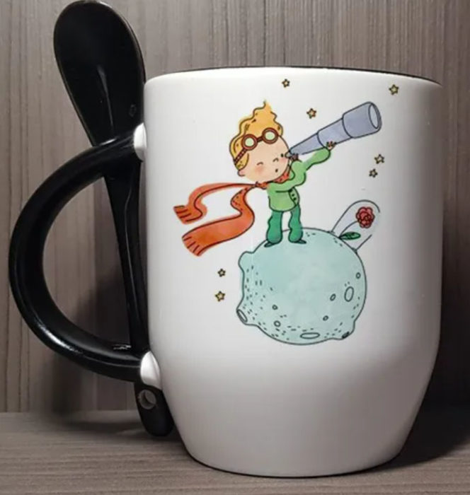 Taza inspirada en El Principito, donde se ve al Principito ver por un telescopio, a su rosa y la cucharita de la taza es negra