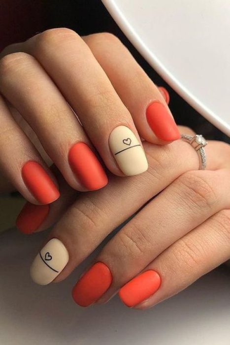 Diseño de manicura en uñas cortas en color rojo con una uña en color beige y detalle en negro en efecto mate