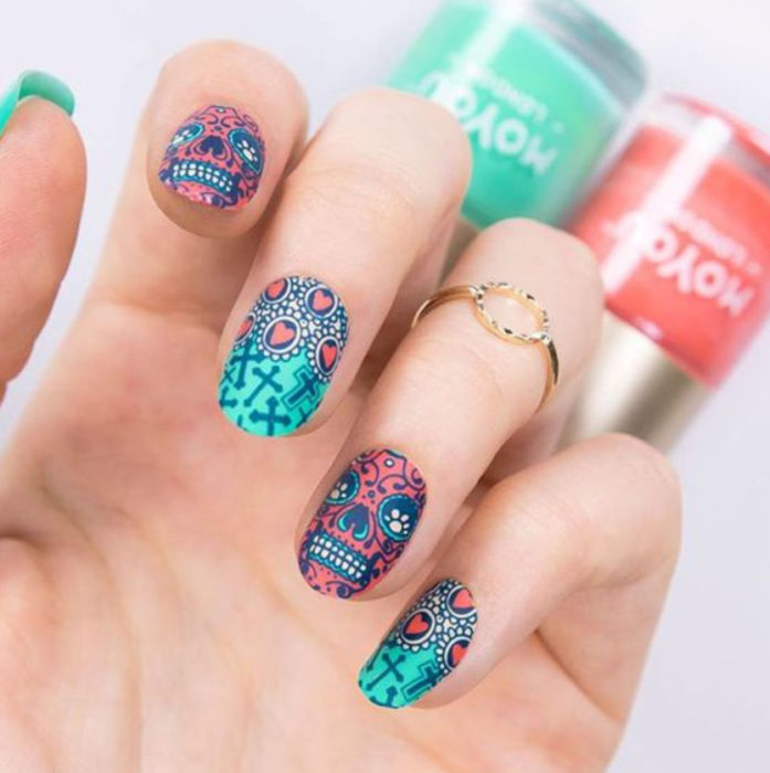 Uñas inspiradas en Día de Muertos con diseño de calaveras, en colores fuccia y verde