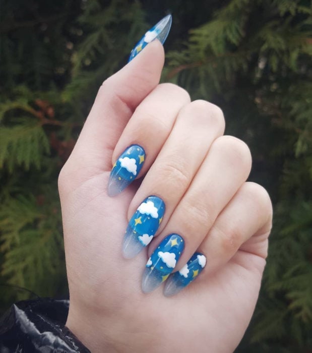 Manicura con diseño de cielo y nubes; uñas largas en forma de almendra pintadas con esmalte azul degradadas a transparente