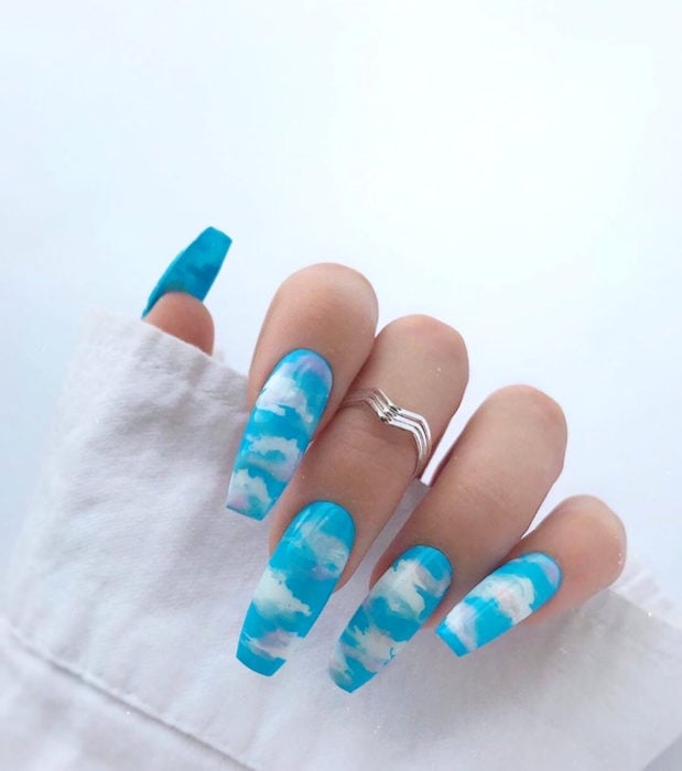 Manicura con diseño de cielo y nubes; uñas largas cuadradas pintadas con esmalte azul bebé