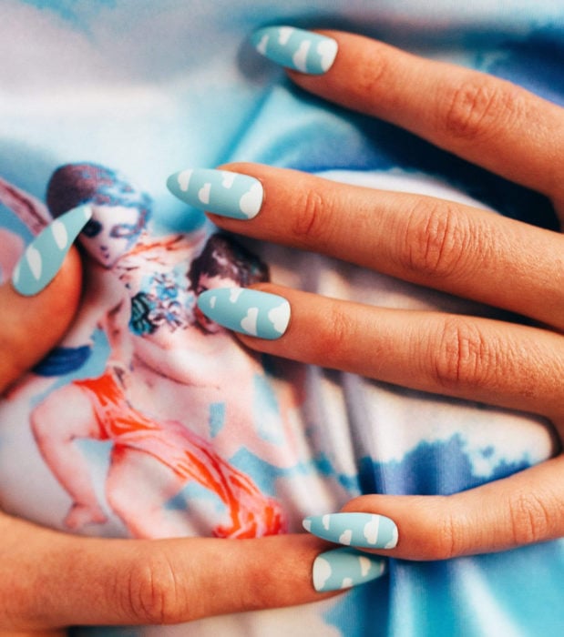 Manicura con diseño de cielo y nubes; uñas largas en forma de almendra pintadas con esmalte azul bebé