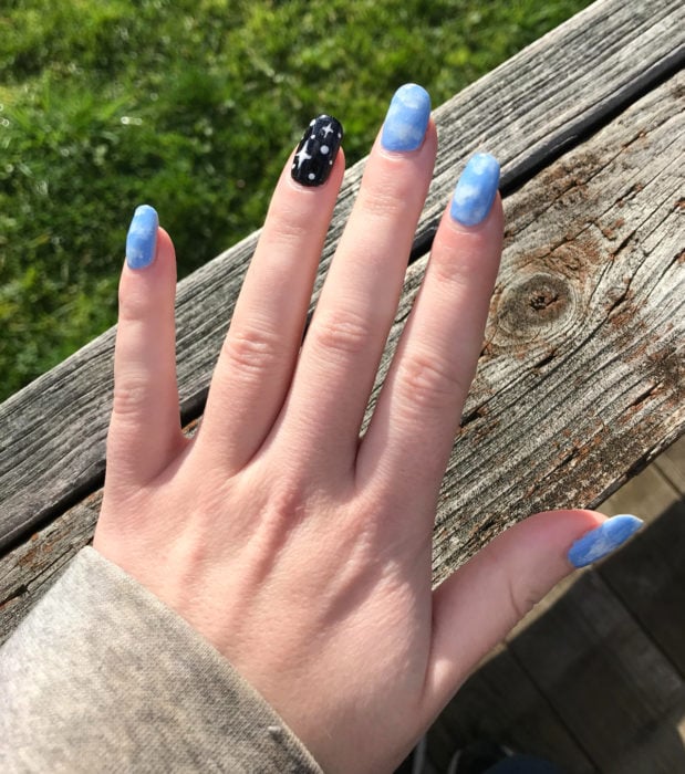 Manicura con diseño de cielo y nubes; uñas cortas cuadradas pintadas con esmalte azul y negro